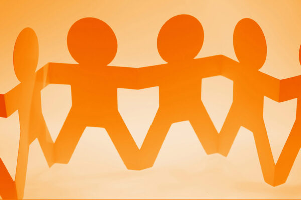 Papierfiguren in orange, die Hand in Hand eine symbolische Gemeinschaft und Zusammenarbeit darstellen.